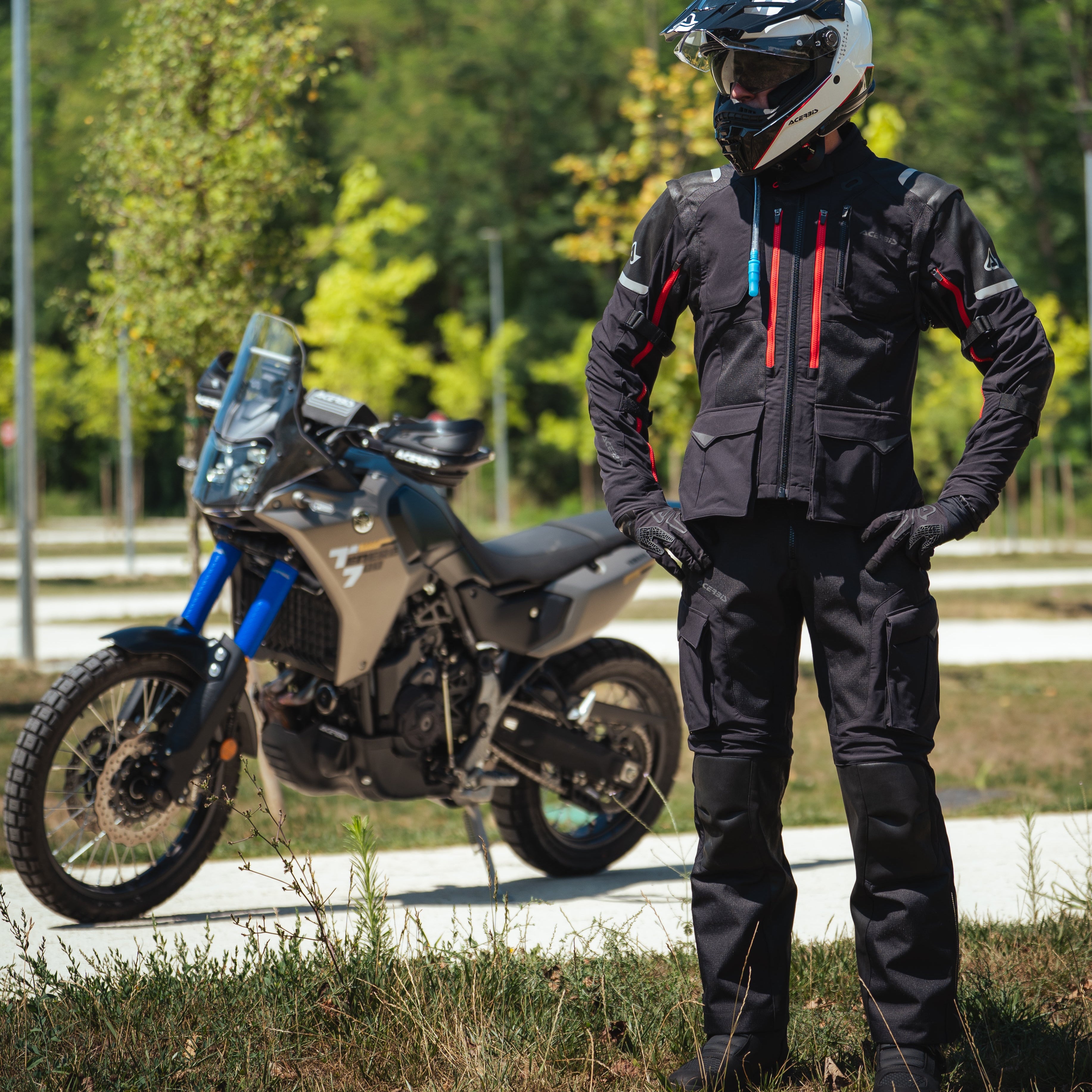 Person in motorcycle gear standing next to a parked motorcycle outdoors.