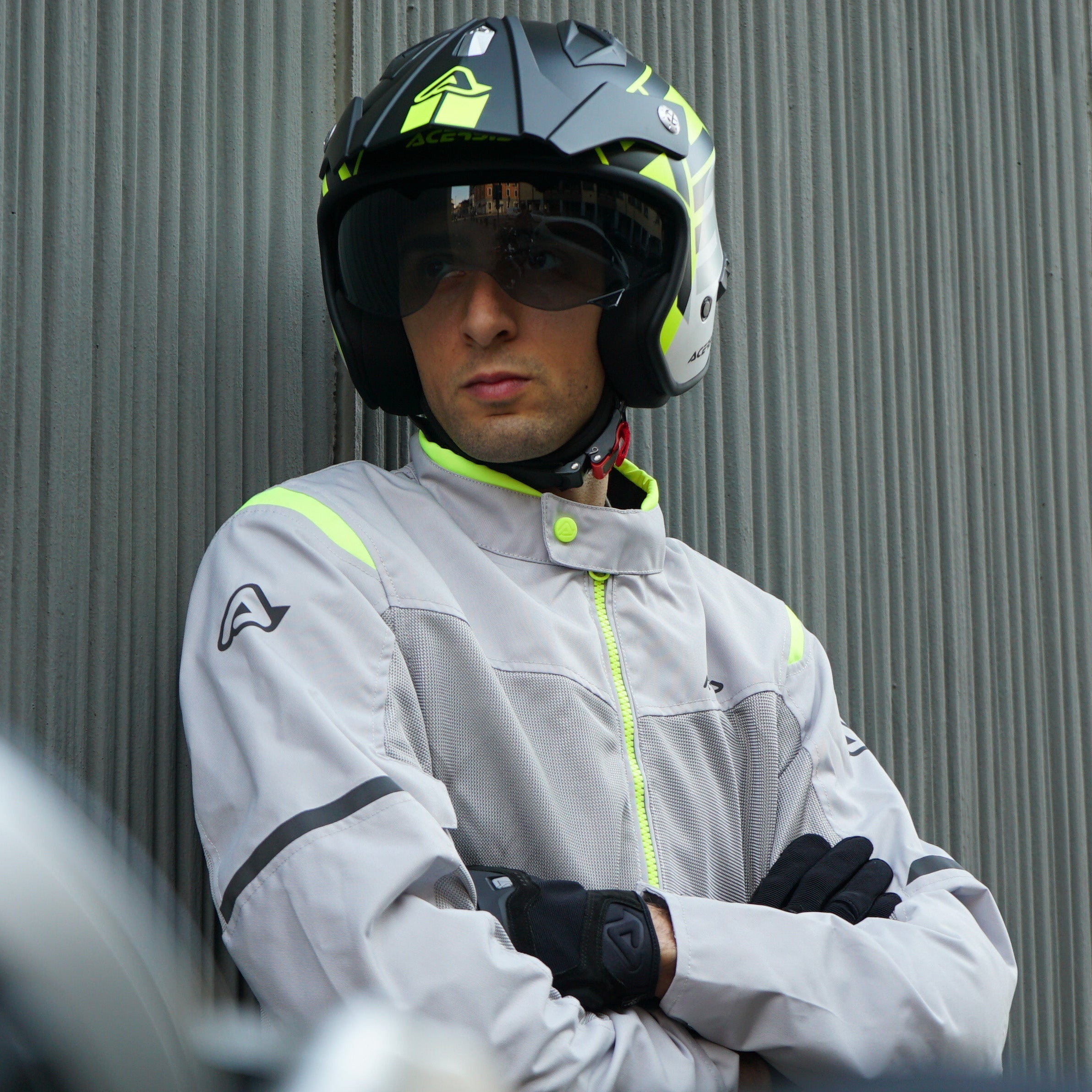 Person wearing a helmet and racing suit standing against a metallic wall.