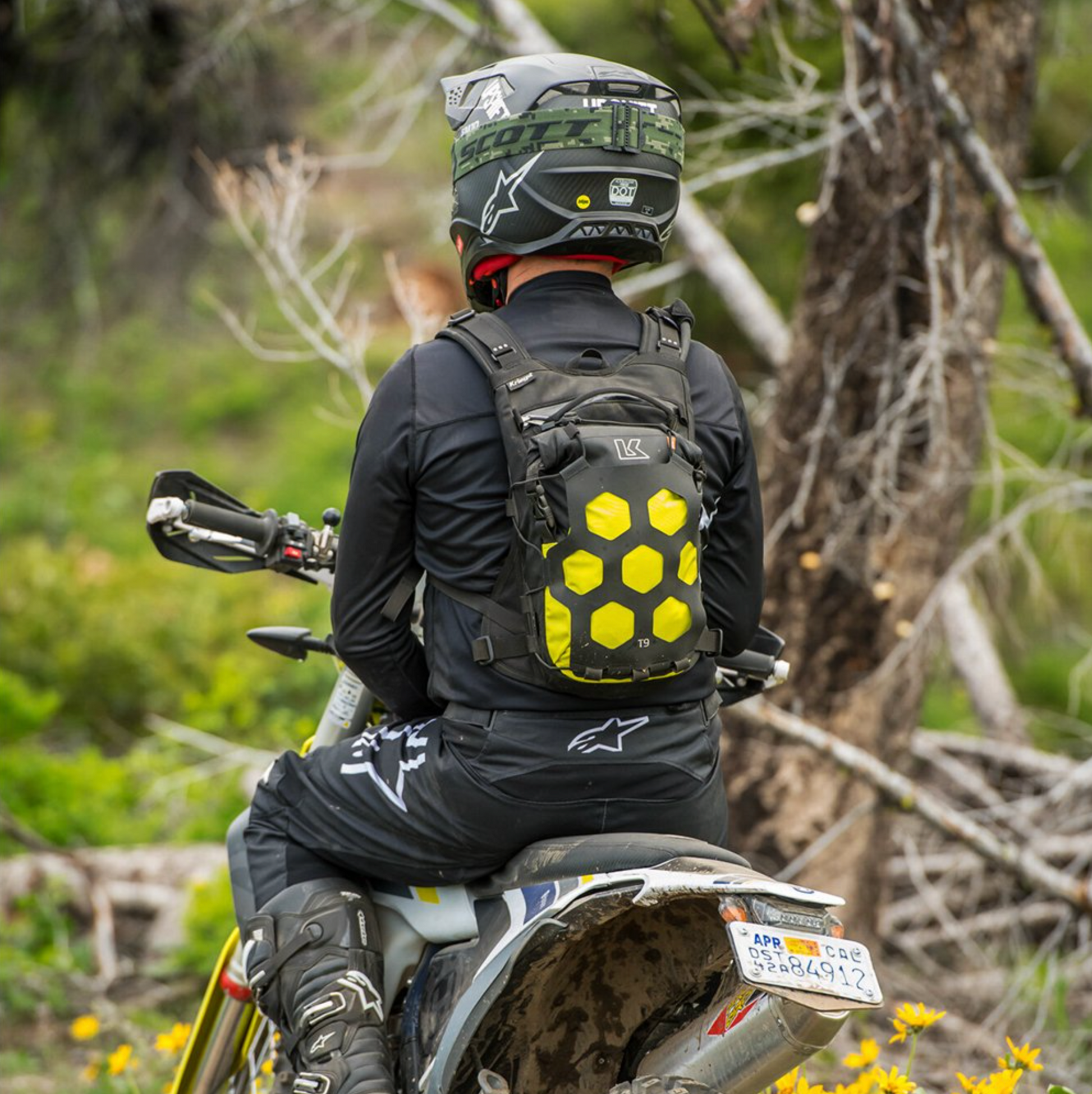 Person on a motorcycle wearing a helmet and carrying a backpack with a forest background