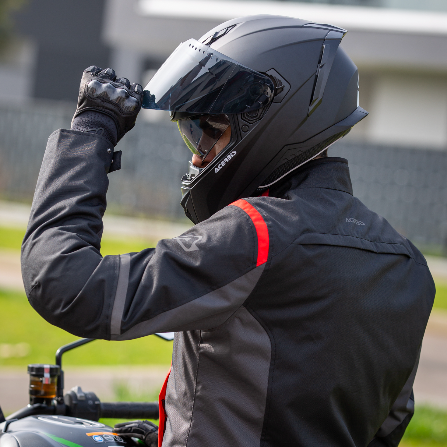 Person wearing a black motorcycle helmet and jacket, sitting on a motorcycle.