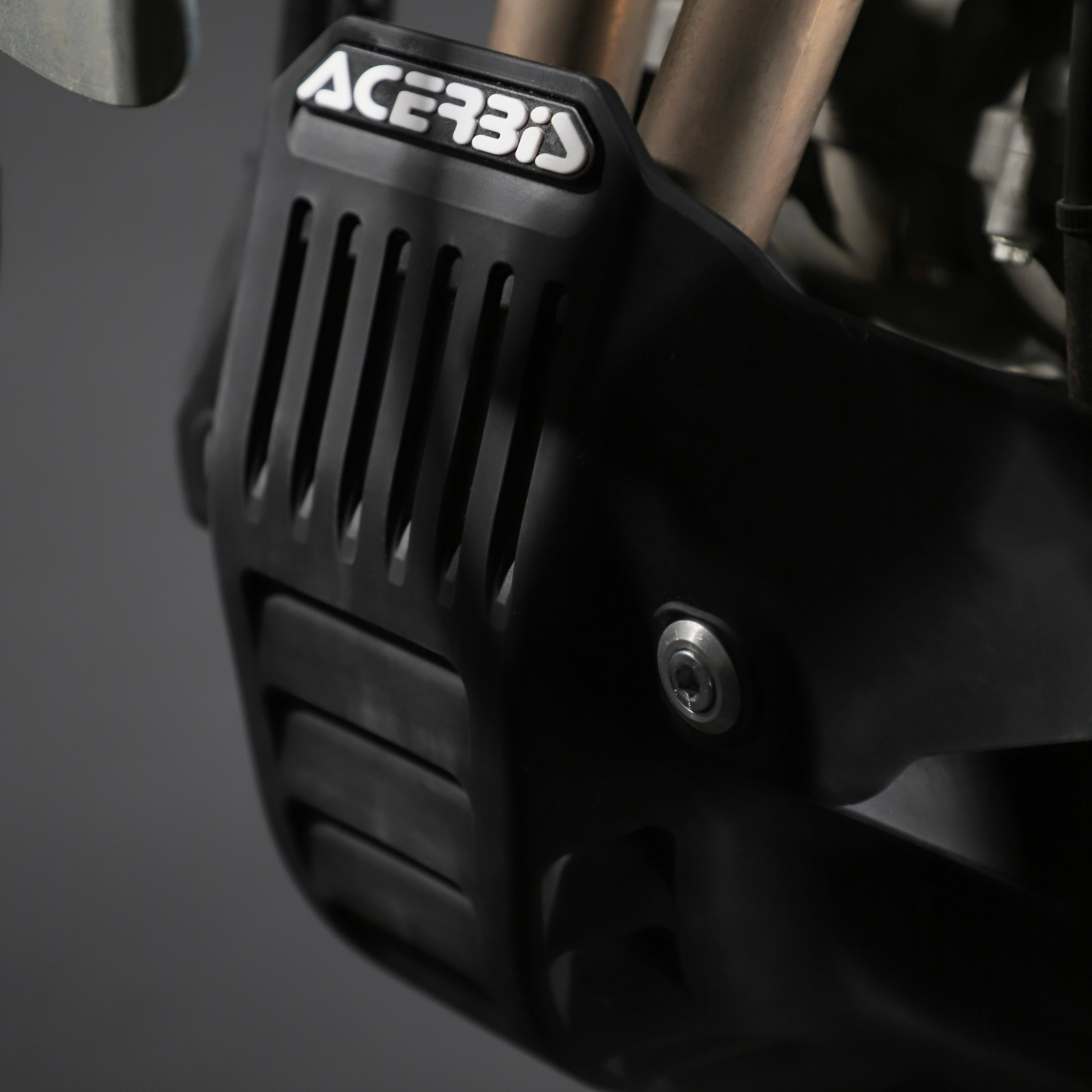 Close-up of a black motorcycle part with 'Acerbis' branding on a dark background
