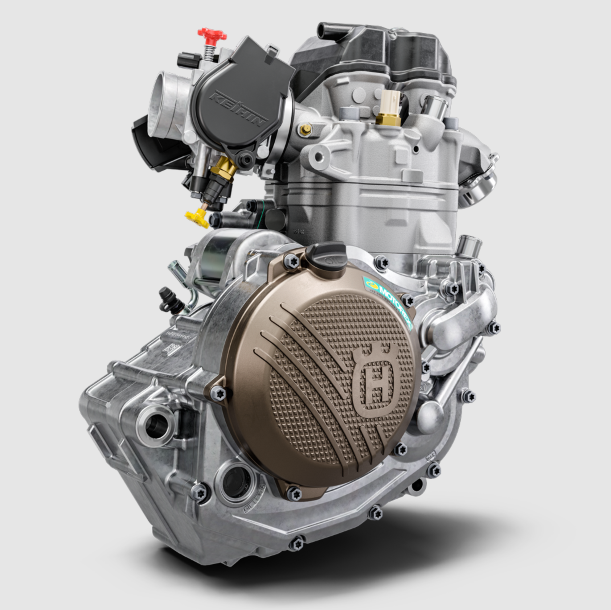 A high-performance motorcycle engine with a silver aluminum body, a prominent bronze-colored crankcase cover, and black components, shown on a light gray background.