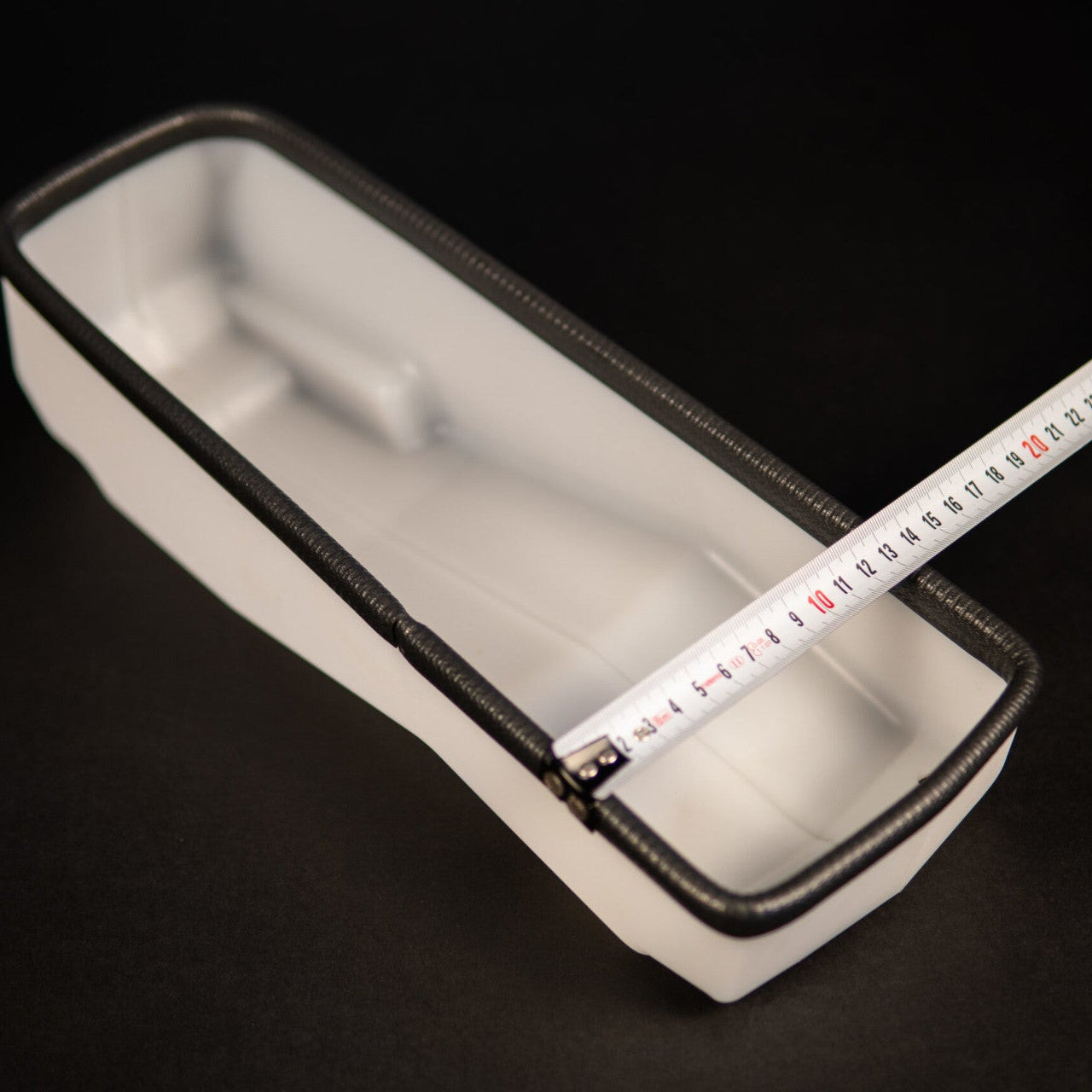 White rectangular container with a black zipper and a measuring tape inside on a black background